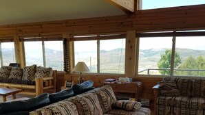 A spacious living room with a large wooden sofa, a smaller sofa, and a wooden coffee table. There are multiple windows providing a view of the mountains. - Come stay at the McMinn Inn and enjoy the mountian views! (Inkom)
