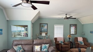 A living room with a brown leather sofa, two brown armchairs, a wooden coffee table, and a ceiling fan.