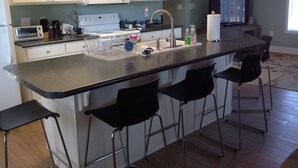 A kitchen with white cabinets, a microwave, a toaster, a sink, and a bar area with stools.