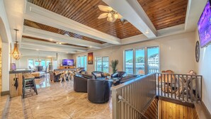 A spacious living area with a high ceiling, a wooden staircase, and a large window offering a view of the outside.