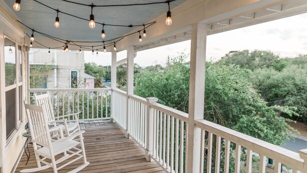 A wooden deck with white railings, string lights, and rocking chairs. - Always a great time on south island of Tybee! and short drive to Savannah! (Tybee Island)