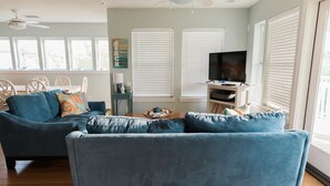 A living room with a blue sofa, a television, and a dining area with a table and chairs. - Always a great time on south island of Tybee! and short drive to Savannah! (Tybee Island)