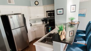 A modern kitchen with white cabinets, stainless steel appliances, a black countertop, and a blue chair. - Always a great time on south island of Tybee! and short drive to Savannah! (Tybee Island)