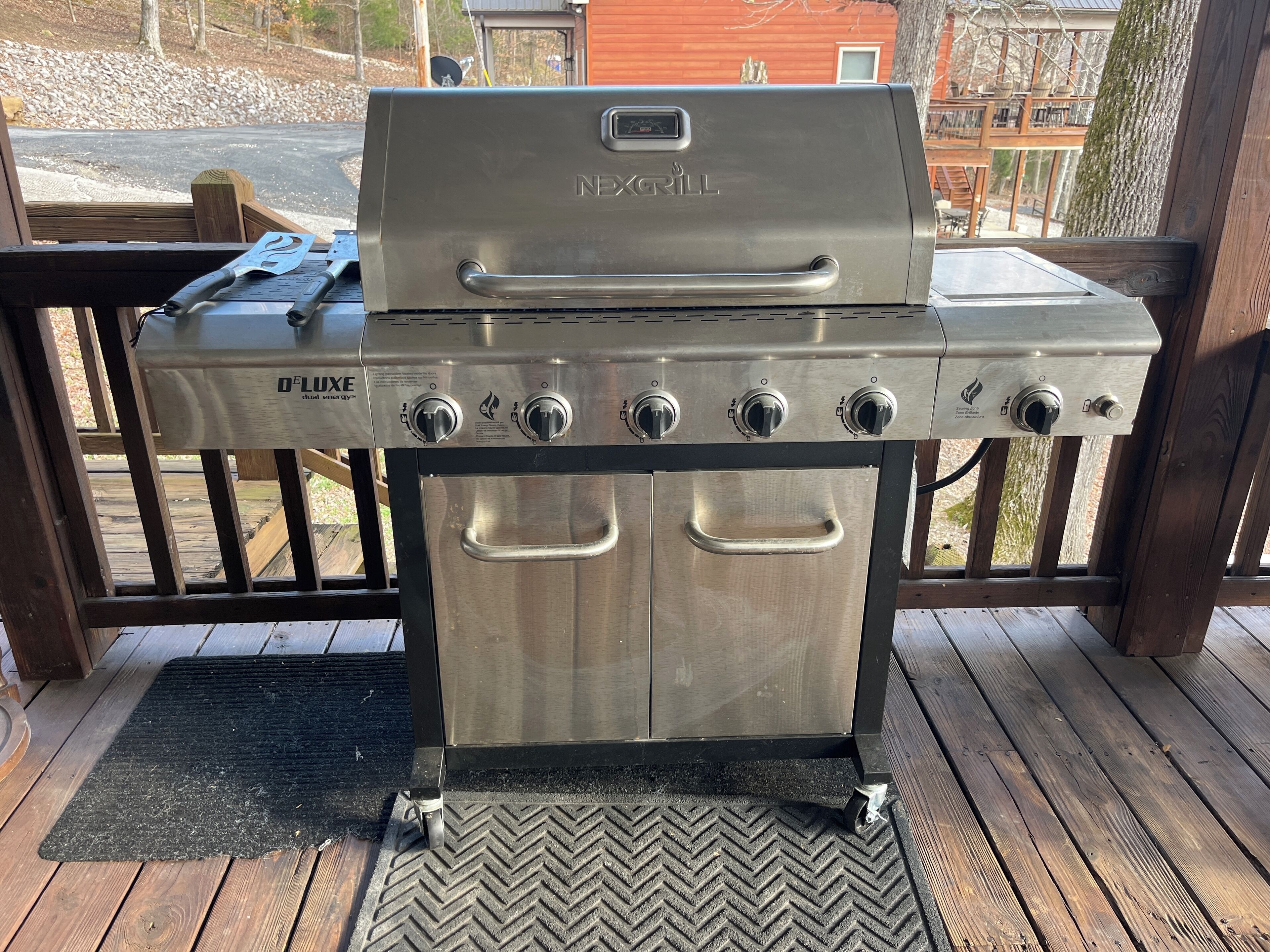 Una griglia NEXGRILL in acciaio inossidabile con display digitale e diverse manopole di controllo, posizionata su un pavimento di legno con motivo a spina di pesce.