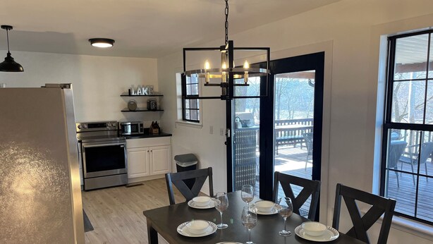 A modern kitchen with stainless steel appliances, a dining table set for six, and a large window overlooking a deck.