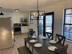 Una cocina moderna con electrodomésticos de acero inoxidable, una mesa de comedor preparada para seis personas y un ventanal con vistas a una terraza.