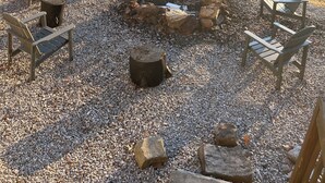 An outdoor seating area with Adirondack chairs and a fire pit surrounded by gravel.