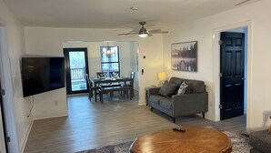 A living room with a TV, a round wooden coffee table, a gray sofa, and a dining area with a table and chairs.