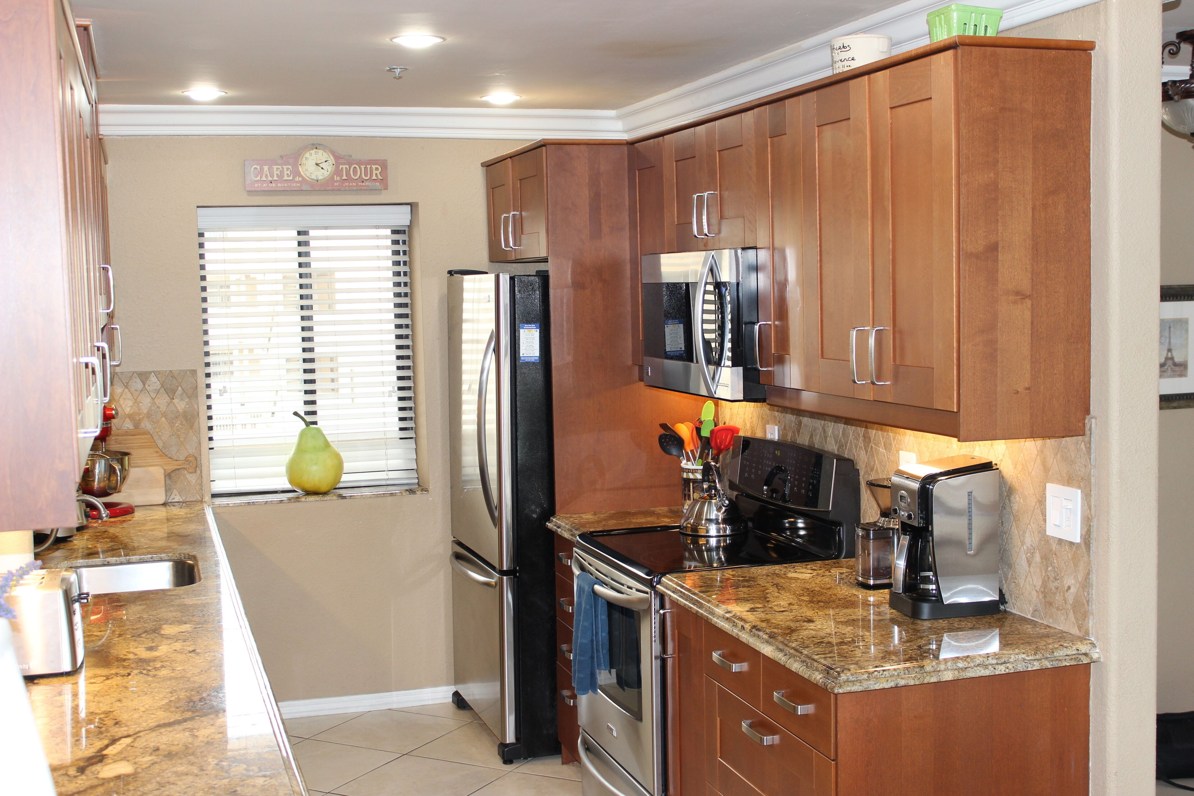 A kitchen with wooden cabinets, stainless steel appliances, a refrigerator, a microwave, a stove, and a window with blinds.