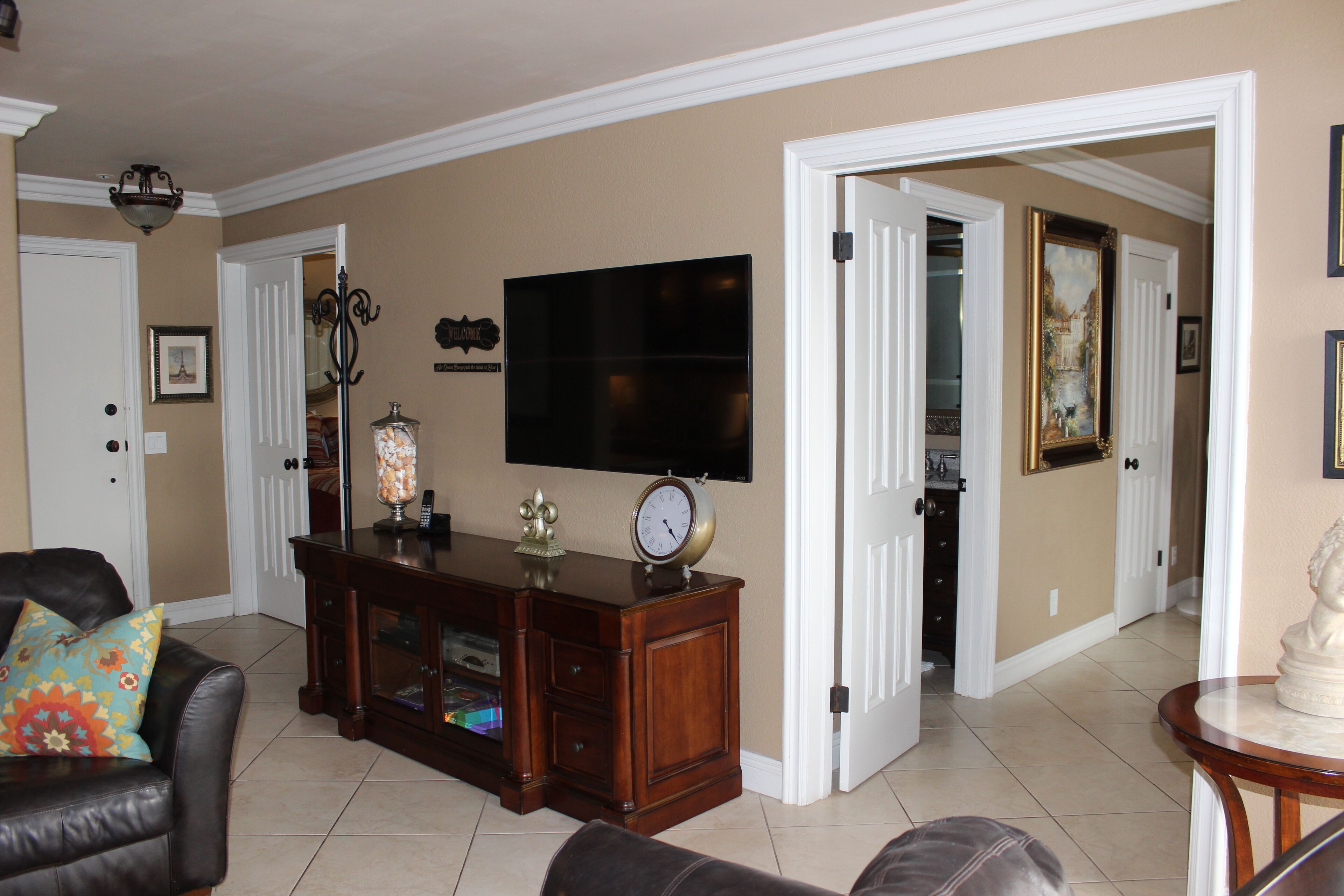 A living room with a dark wooden entertainment center, a flat-screen TV, and a clock. There is a door leading to another room.