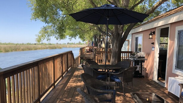 A wooden deck with wicker furniture and a table, overlooking a body of water.