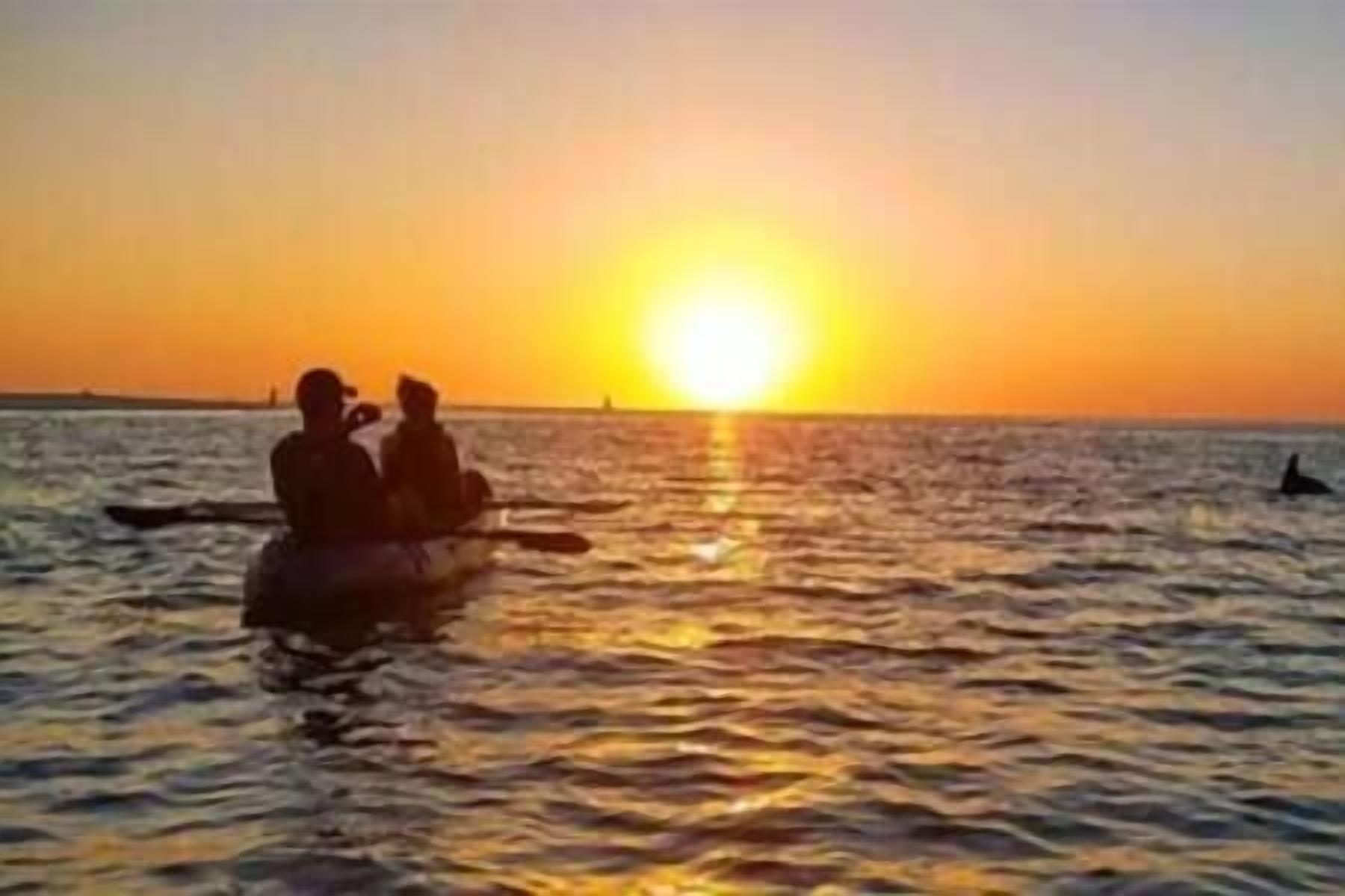 Un atardecer sobre una masa de agua con dos personas en un bote.