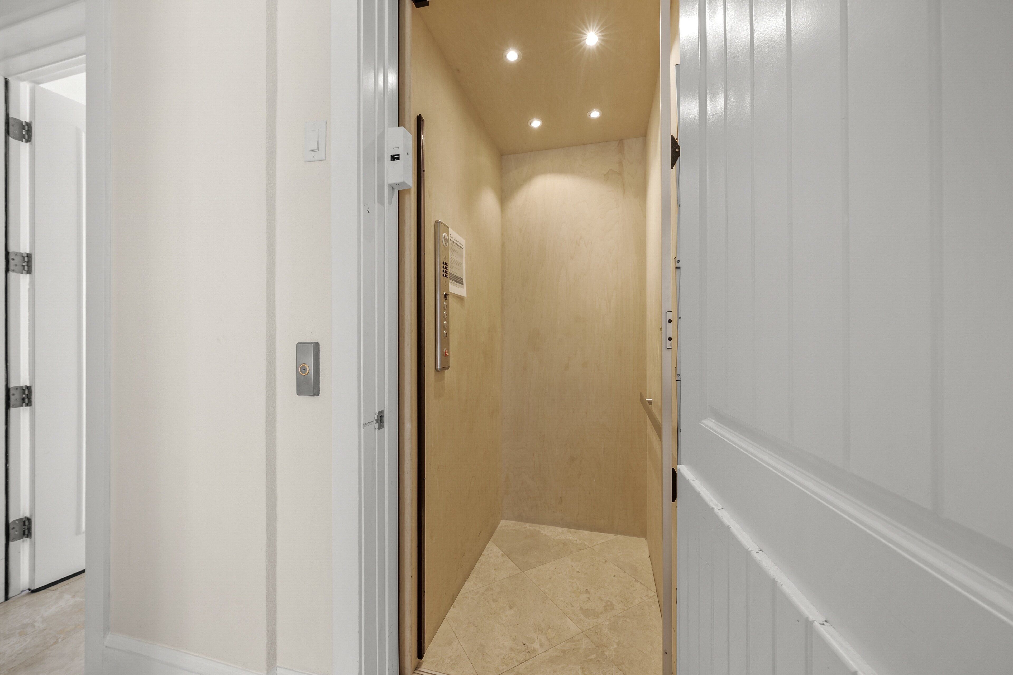 A narrow hallway with a door leading to a room with a tiled floor and a ceiling light fixture.