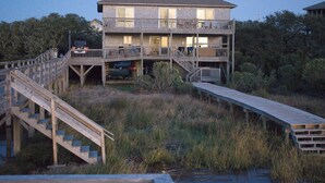 A two-story wooden building with a balcony on the upper floor, a staircase leading to the upper level, and a wooden dock extending into a body of water. - SOUND FRONT!, Kite-In/Out! Sunsets! Dock!  (Salvo)