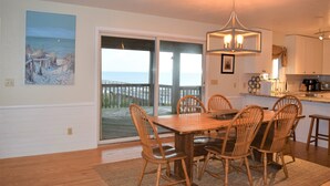 A dining area with a wooden table and chairs, a chandelier, and a view of the ocean through a sliding glass door. - SOUND FRONT!, Kite-In/Out! Sunsets! Dock!  (Salvo)