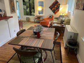 Un área de comedor con una mesa preparada para cuatro personas, rodeada de sillas, un sofá y una lámpara.