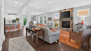 Una sala de estar moderna con chimenea, televisor y cocina al fondo.