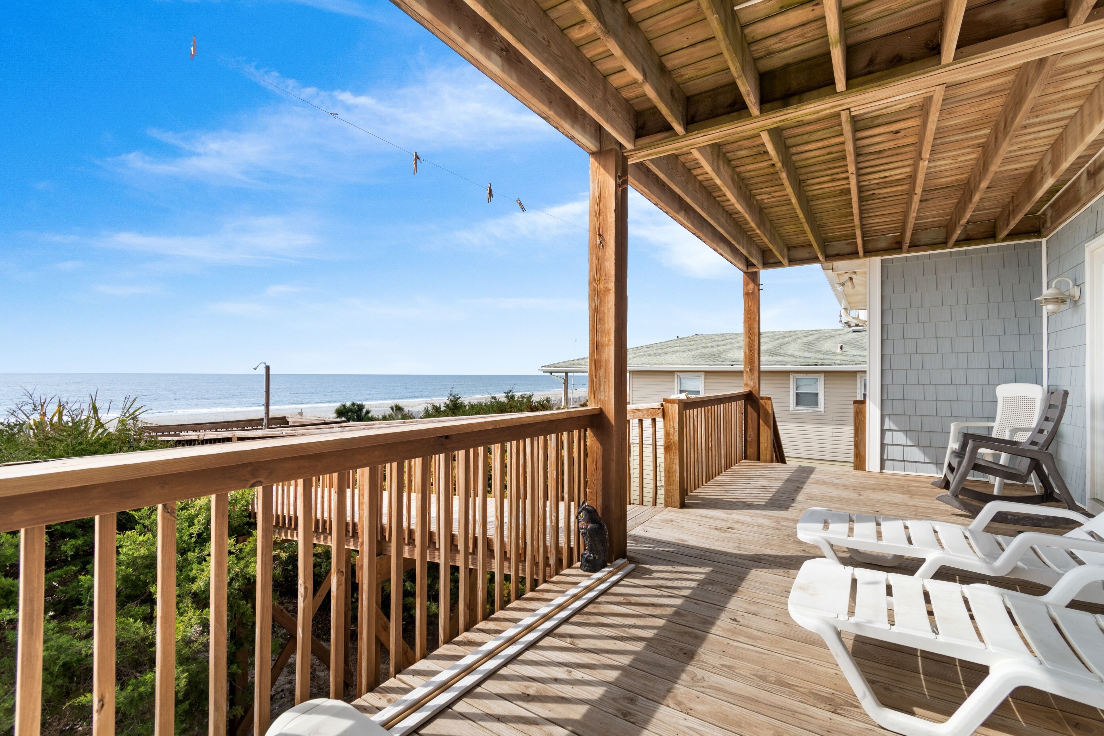 A wooden deck with white lounge chairs, a wooden railing, and a view of the ocean.