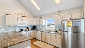 A modern kitchen with white cabinets, a stainless steel refrigerator, and a granite countertop. - "Oceans Edge" - Luxury Oceanfront home, 4 Bedrooms / 2.5 Bathrooms (Holden Beach)