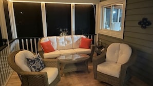 Une véranda aménagée avec des meubles en osier, notamment un canapé et deux fauteuils, ainsi qu’une petite table ronde.