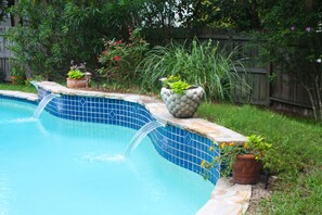 Ein Schwimmbecken mit Fliesenrand, umgeben von Kübelpflanzen und einem Holzzaun.