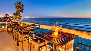 An outdoor dining area with tables and chairs overlooking a beach and ocean at sunset. - Oceanfront Beach, Pool, Hot Tub, Pickleball, Movie Theater, Elevator & Golf Cart (La Jolla)