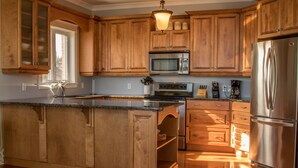 A kitchen with wooden cabinets, a stainless steel refrigerator, a built-in microwave, and a granite countertop. -  Walk to Fine Restaurants & Confederation Centre of The Arts. (Charlottetown)