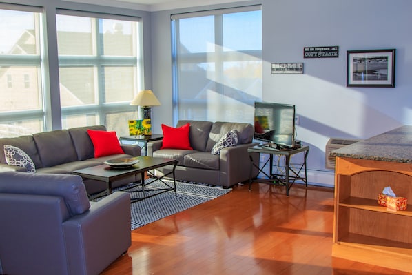 A modern living room with a grey sofa set, a coffee table, a TV on a stand, and a wooden sideboard.