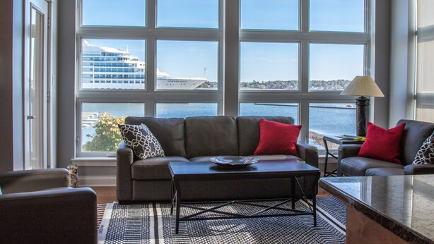 A living room with a large window overlooking a body of water and a building. There is a sofa, a coffee table, and a lamp. -  Walk to Fine Restaurants & Confederation Centre of The Arts. (Charlottetown)