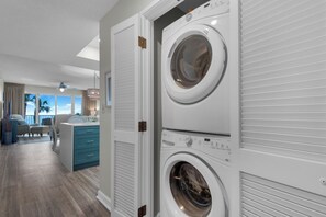 A laundry room with two front-loading washing machines, a blue cabinet, and a view of a balcony with outdoor furniture.