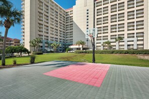 A basketball court with a red key area, surrounded by a building with multiple balconies and palm trees. - Gulf-Front Tides Unit 202 | 2BR | Sleeps 6 (Miramar Beach)