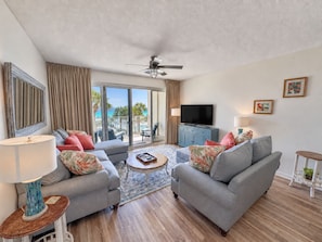 A living room with two sofas, a coffee table, a TV, and a balcony with a view.