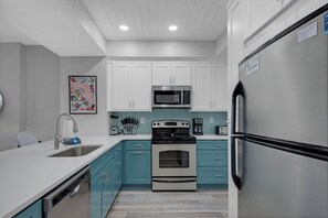 A kitchen with white cabinets, a stainless steel refrigerator, a microwave, a stove, and a sink.