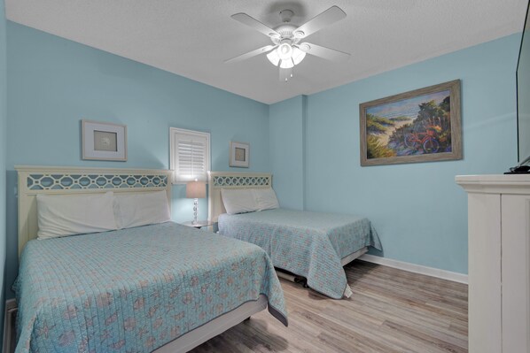 A bedroom with two beds, a ceiling fan, a painting, and a window with blinds. - Gulf-Front Tides Unit 202 | 2BR | Sleeps 6 (Miramar Beach)