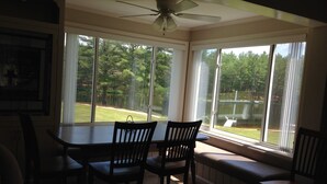 A dining area with a table and chairs, large windows with a view of a yard and trees, and a ceiling fan. - Beautiful Farmhouse located on 1200 acres of private bliss with a quiet pond. (Brownfield)