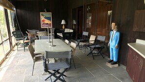 An outdoor seating area with stone flooring, wicker chairs, and a table. A mannequin in a blue suit stands to the right. - Quiet, Private Lakefront Cottage - Skaneateles Lake (Homer)