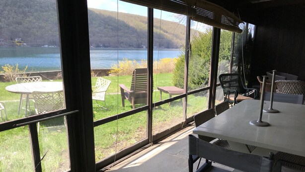 A covered outdoor seating area with a table and chairs, overlooking a lake and hills. - Quiet, Private Lakefront Cottage - Skaneateles Lake (Homer)