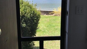 A door with a view of a lake, grassy area, and trees. - Quiet, Private Lakefront Cottage - Skaneateles Lake (Homer)