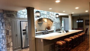 Een keuken met een achterwand van steen, een groot eiland met barstoelen en een inbouwoven.