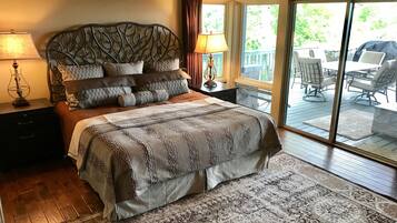 A bedroom with a large bed, a nightstand, a lamp, and a view of an outdoor patio with chairs and a table.
