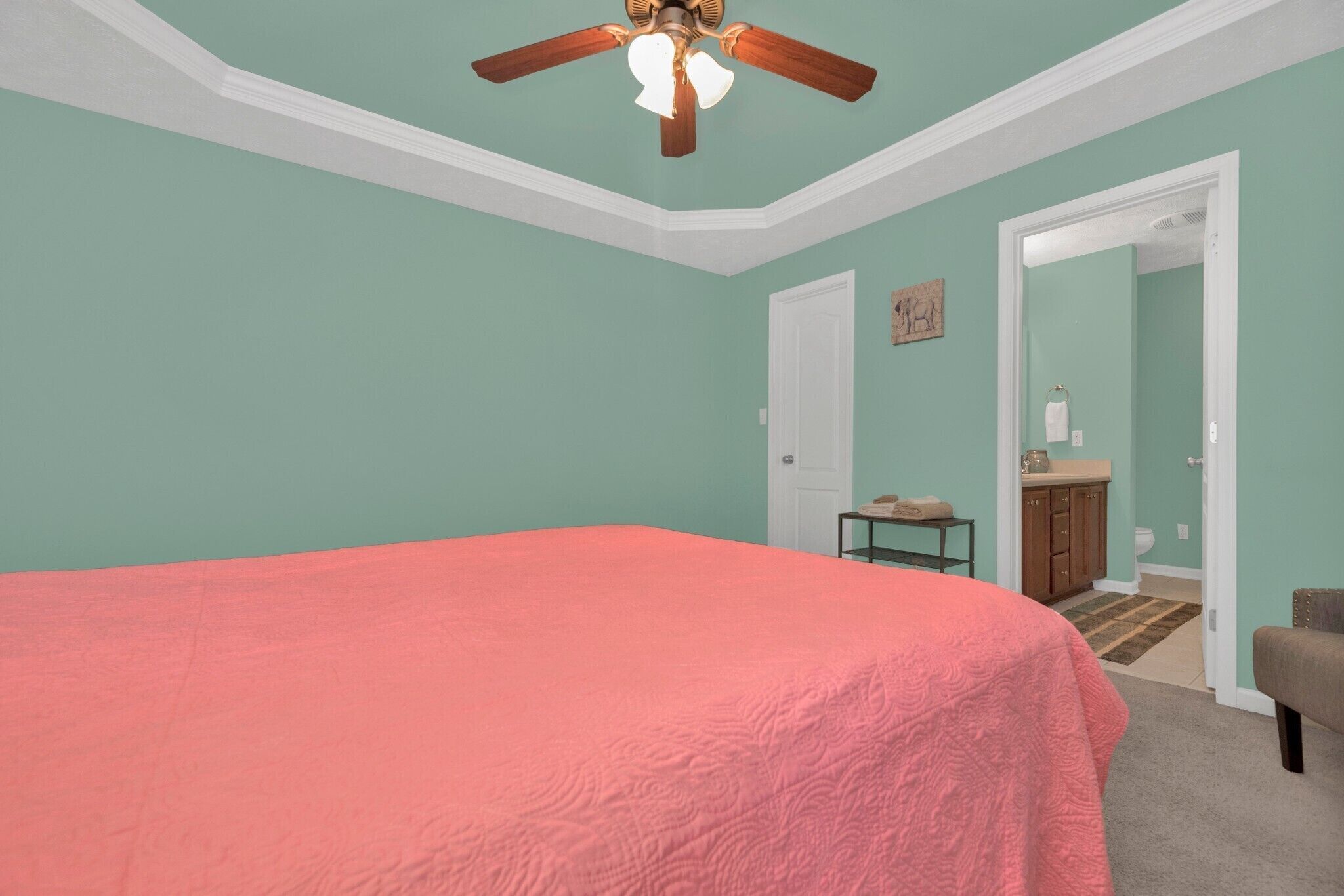 Un dormitorio con una cama grande, un ventilador de techo y una puerta que da al baño.