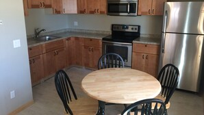 Una cocina con armarios de madera, microondas, estufa, refrigerador y una mesa redonda de madera con cuatro sillas.