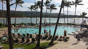 A pool area with lounge chairs and umbrellas, surrounded by palm trees and a view of the ocean.