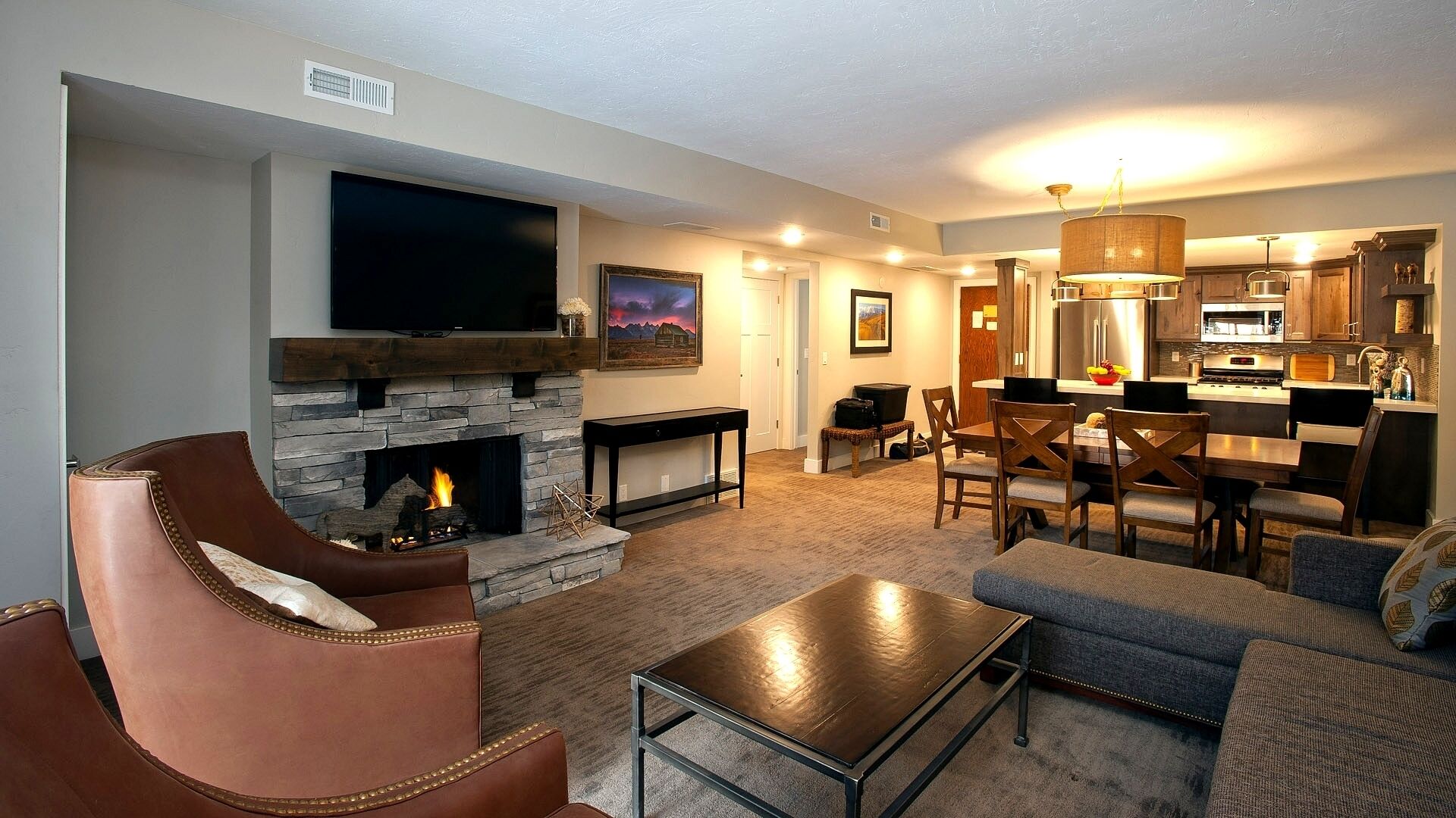 Een woonkamer met een stenen openhaard, een flatscreen-televisie, leren fauteuils en een eethoek met houten stoelen en een tafel.