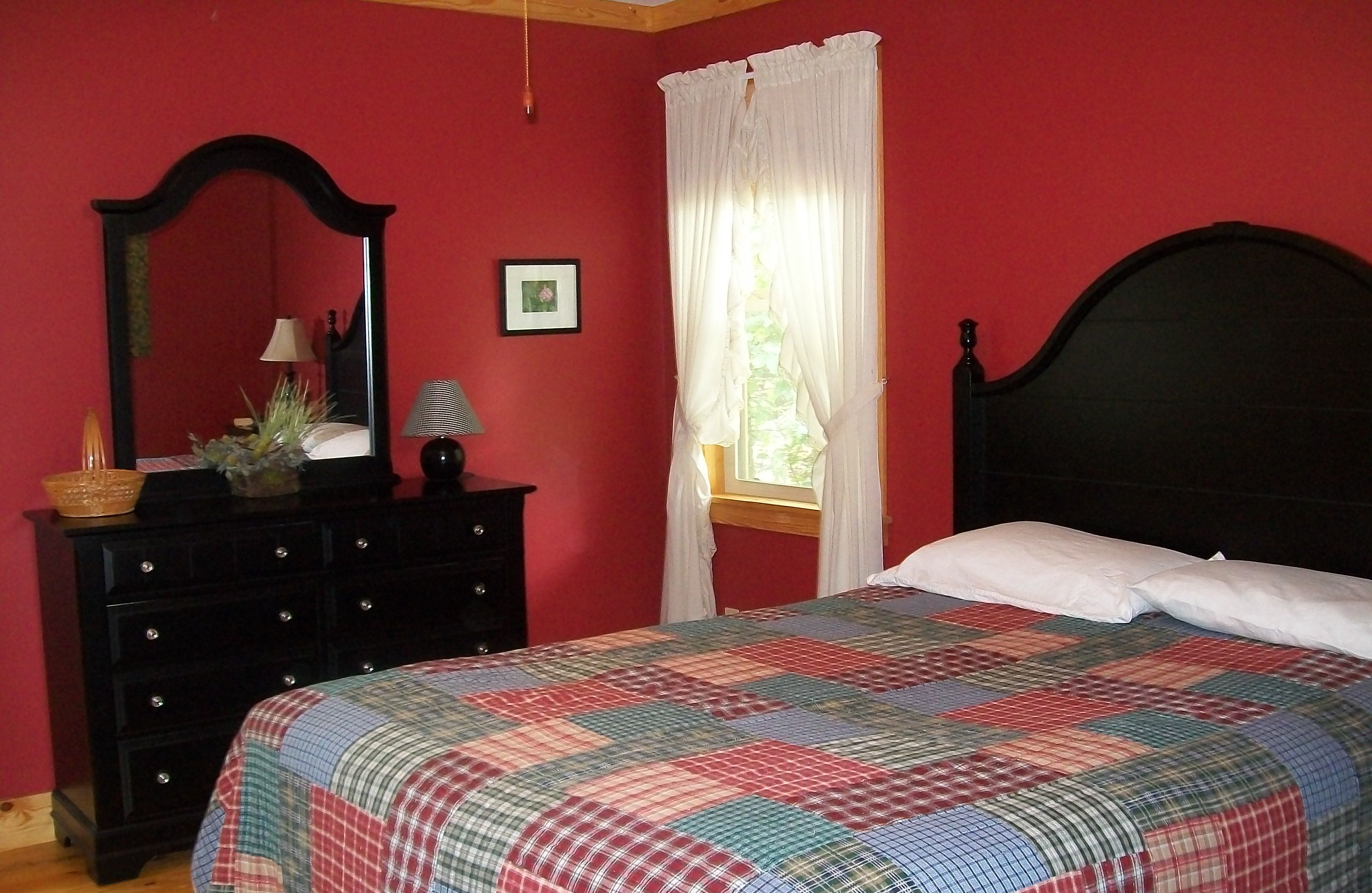 A bedroom with a bed, a dresser, a mirror, and a window with curtains.