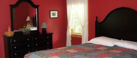 A bedroom with a bed, a dresser, a mirror, and a window with curtains.