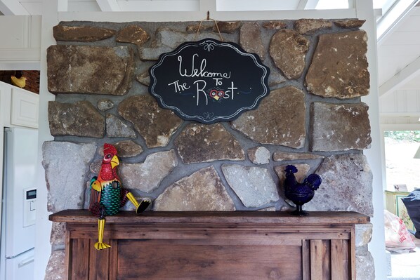 A stone wall with a welcome sign and two decorative roosters.
