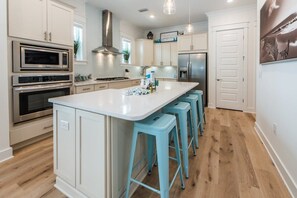 Una cocina moderna con armarios blancos, electrodomésticos de acero inoxidable y una isla central con taburetes de bar.