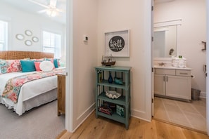 Un dormitorio con cama, mesita de noche, estante en la pared y baño con lavamanos y espejo.