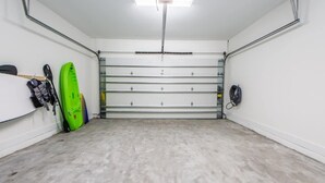 Siisti, tyhjä autotalli, jossa on betonilattia, vihreä kajakki ja seinää vasten nojaava suppilauta.